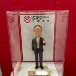 一款贈予工銀亞洲 (ICBC Asia) 員工的榮休禮物。這款人像公仔被放置在刻有「Happy Retirement 2025」的亞加力膠展示盒中，背景是工銀亞洲的公司標識。