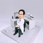 醫生人像公仔，身穿白色醫生袍，端坐在診症室內黑色椅子上，身後擺放電腦螢幕與醫療儀器，桌上可見檢測設備與辦公用具，呈現專業醫護場景。此專屬訂製人像公仔適合作為醫生禮物、醫護退休紀念、升職賀禮或醫療團隊專屬收藏。