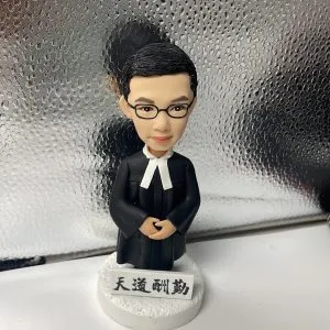 一款男性律師人像公仔，身穿律師袍，站立在刻有「天道酬勤」銘牌的底座上，是送給律師的完美入職禮物。