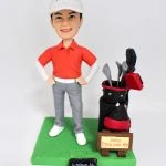 手工製作的高爾夫球運動人像公仔，穿著紅色球衣與白色帽子，身旁搭配精緻高爾夫球桿袋，展現運動熱情與專屬個人風格，為高爾夫球愛好者打造獨一無二的專屬紀念品。