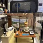 訂製醫生人像公仔｜教授坐於辦公桌前，桌面擺放電腦滑鼠、筆、紙張與個人照片，背景還原窗外大學醫院景觀，桌邊配有醫療監測儀器與實驗設備，展現醫護專業氛圍與退休紀念禮物的獨特價值。