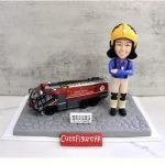 一款為機場消防員訂製的退休人像公仔，公仔身穿全套消防制服，旁邊停放著一輛香港國際機場的專用消防車模型，底座銘牌刻有贈予總隊目何耀平的退休祝福。