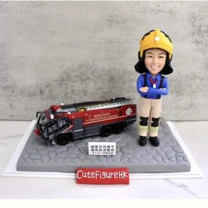 一款為機場消防員訂製的退休人像公仔,公仔身穿全套消防制服,旁邊停放著一輛香港國際機場的專用消防車模型,底座銘牌刻有贈予總隊目何耀平的退休祝福。