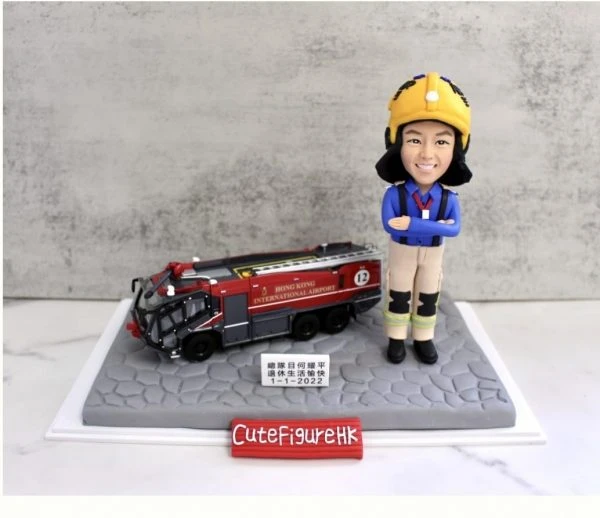 一款為機場消防員訂製的退休人像公仔，公仔身穿全套消防制服，旁邊停放著一輛香港國際機場的專用消防車模型，底座銘牌刻有贈予總隊目何耀平的退休祝福。