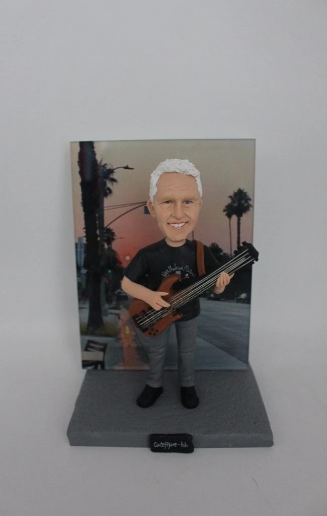 一款為外國同事訂製的生日禮物人像公仔，描繪了一位白髮男士正在彈奏低音結他，身後有加州日落街景的照片背景。