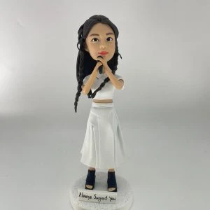 一款留有黑色長編髮的女歌手人像公仔，她身穿全白套裝，雙手握著咪高峰，站立在一個寫有 "Always Support You" 的白色圓形地台上。