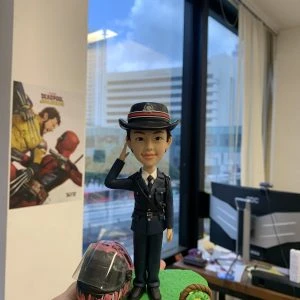 以立正敬禮定格專業形象：這款警察人像公仔以深藍制服與帽徽為主角，肩帶、口袋與鈕扣層次分明；臉部眉眼與笑意弧度、髮際線皆以手工刻線呈現。底座採草地質感，搭配塗裝安全頭盔與編織籃等客製小物，強化角色故事性。無論升遷誌慶、部門感謝或退休紀念，皆是充滿心意的送禮之選。