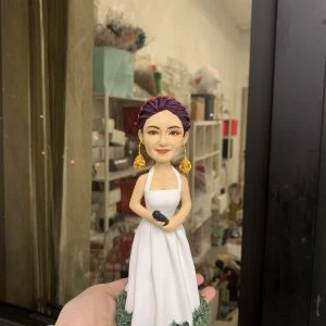 一款為擁有紫色編髮造型的女歌手訂製的人像公仔，她身穿白色長裙，配戴金色玫瑰耳環，手持咪高峰，並站立在一個綠色草地底座上。
