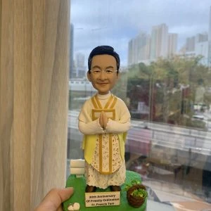一款神父人像公仔，為慶祝晉鐸30週年而設，公仔身穿禮儀祭衣，底座刻有紀念字句，是一份送給牧師或神職人員的禮物。