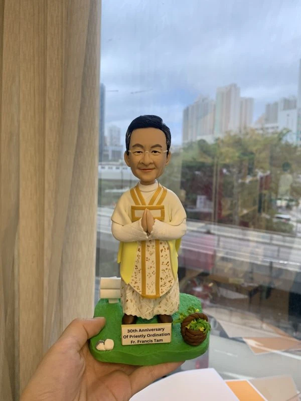 一款神父人像公仔，為慶祝晉鐸30週年而設，公仔身穿禮儀祭衣，底座刻有紀念字句，是一份送給牧師或神職人員的禮物。