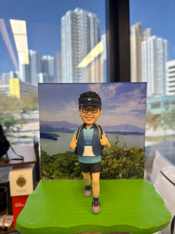 越野跑手人像公仔，戴著黑色帽子與眼鏡，身穿運動背心、短褲與登山鞋，背著背包踏步向前。背景是山脈與湖泊風景，展現戶外越野長跑的熱情與活力。