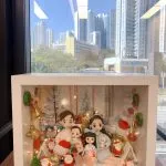 手工製作的 人像公仔 場景作品，裝在透明展示盒中，呈現一家四口的溫馨畫面。父母與兩個小孩坐在一起，背景裝飾有聖誕樹、金色小熊、禮物盒及多個聖誕老人公仔，搭配燈飾與紅色毛帽小物，營造節日氛圍。此作品結合 家庭團聚 與 聖誕節禮物 主題，展現專屬紀念與溫馨心意。