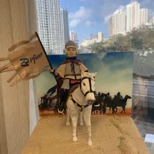 英勇騎士主題人像公仔，身穿盔甲與斗篷的男性公仔騎乘白馬，手持印有 Pfizer 標誌的旗幟，背景為沙場戰馬場景。整體設計充滿英勇與榮耀氛圍，專為老闆退休製作的獨特禮物。