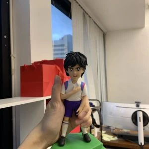 一款根據經典動漫人物《足球小將》戴志偉製作的人像公仔，公仔身穿球衣，手撫胸口，是送給粉絲的完美生日禮物。