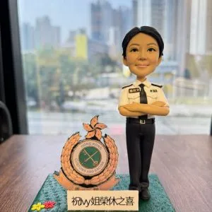 「香港海關人像公仔，身穿白色制服襯衫與黑色長褲，雙手交叉胸前，神情自信專業。底座展示『Hong Kong Customs and Excise』徽章，以及『祝 Ivy 姐榮休之喜』字樣，象徵此公仔為慶祝香港海關職員榮休（退休）特別訂製的專屬紀念禮物。此公仔細節精緻，適合作為榮休禮物、警察或海關紀念品，以及專屬人像公仔收藏。」