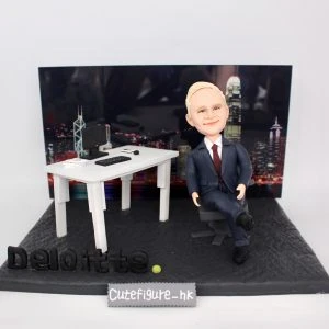一款為外國老闆訂製的退休禮物人像公仔,公仔是一位穿西裝的男士,坐在辦公室的立體場景中,背景是香港維港背景夜景,底座上有Deloitte公司標誌。