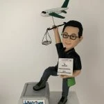 一款為國泰航空地勤營運人員訂製的15週年紀念人像公仔，主角手持飛機裝卸手冊，並舉著一個帶有飛機模型與天秤的背景配件裝飾。