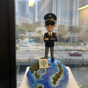 一款為機師退休設計的人像公仔，公仔身穿機師制服、戴太陽眼鏡，充滿自信地站在地球模型上，底座寫有「Happy Retirement 2024」，是完美的機師退休禮物。