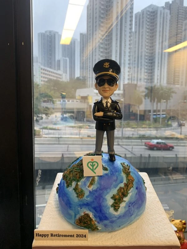 一款為機師退休設計的人像公仔，公仔身穿機師制服、戴太陽眼鏡，充滿自信地站在地球模型上，底座寫有「Happy Retirement 2024」，是完美的機師退休禮物。