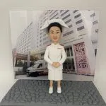 一款為廣華醫院護士訂製的退休禮物。精緻的人像公仔身穿傳統的白色護士服與護士帽，莊重地站立著，背景板是廣華醫院大樓及門前的救護車，是一份完美展現其職業生涯的紀念品。