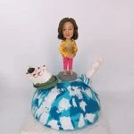 一款送給外國同事的退休禮物，一位女士人像公仔站在地球模型上，地球上有香港的天星小輪模型和新加坡的魚尾獅模型，象徵著兩地的美好回憶。