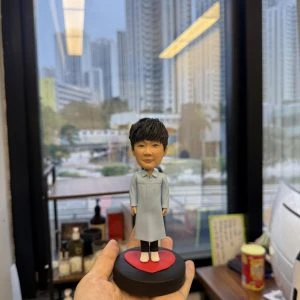 單人宗教人像公仔立於黑色圓形底座上的紅色愛心平台：公仔穿淡藍長袍、深色長褲與白色球鞋，短黑髮、微笑神情。整體造型清新，適合作為洗禮禮物或信仰紀念的人像公仔。