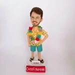 一款為外國同事訂製的人像公仔禮物，公仔是一位戴眼鏡的男士，穿著黃色夏威夷襯衫和戴著花環，站在一個寫有「ALOHA」的沙灘造型底座上。