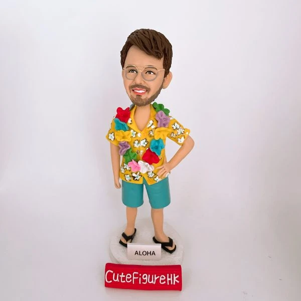 一款為外國同事訂製的人像公仔禮物，公仔是一位戴眼鏡的男士，穿著黃色夏威夷襯衫和戴著花環，站在一個寫有「ALOHA」的沙灘造型底座上。