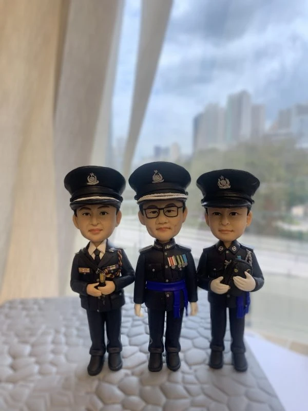 一款為三位高級警務人員訂製的晉升或退休禮物，包含三個身穿警隊禮服的人像公仔，站立在香港警察總部背景前，旁邊有一輛黑色座駕模型車。