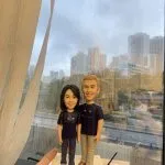 雙人牧師人像公仔：兩位人物並肩貼近、自然微笑，穿深紫團體T恤與休閒長褲；女方配白色運動鞋、男方配棕色皮鞋。立於長方形可刻經文與祝福文字的底座，適合作為教會致謝、授職、周年或生日的人像公仔禮物。