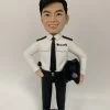 這是一份意義非凡的【晉升】賀禮，為一位年輕的【警務人員】訂製的專屬【人像公仔】。 從公仔的制服細節——尤其是肩上的一條銀色橫柴——我們可以推斷，這位【警務人員】榮升的職位是「見習督察」，這是其警隊生涯一個光輝的起點。公仔自信的笑容與輕鬆的站姿，正是這份喜悅的最佳寫照。 作品設計簡潔而專注，將所有焦點都集中在主角身上，底座的小花點綴，則象徵著他未來職業道路的無限生機。 這份禮物不僅僅是一件擺設，它更是一份認可、一個見證，紀念著他通過努力，成功邁入警官行列的決定性時刻。