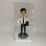 這是一份意義非凡的【晉升】賀禮，為一位年輕的【警務人員】訂製的專屬【人像公仔】。 從公仔的制服細節——尤其是肩上的一條銀色橫柴——我們可以推斷，這位【警務人員】榮升的職位是「見習督察」，這是其警隊生涯一個光輝的起點。公仔自信的笑容與輕鬆的站姿，正是這份喜悅的最佳寫照。 作品設計簡潔而專注，將所有焦點都集中在主角身上，底座的小花點綴，則象徵著他未來職業道路的無限生機。 這份禮物不僅僅是一件擺設，它更是一份認可、一個見證，紀念著他通過努力，成功邁入警官行列的決定性時刻。