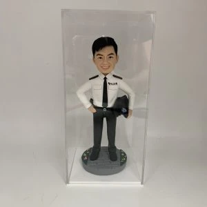 這是一份意義非凡的【晉升】賀禮，為一位年輕的【警務人員】訂製的專屬【人像公仔】。 從公仔的制服細節——尤其是肩上的一條銀色橫柴——我們可以推斷，這位【警務人員】榮升的職位是「見習督察」，這是其警隊生涯一個光輝的起點。公仔自信的笑容與輕鬆的站姿，正是這份喜悅的最佳寫照。 作品設計簡潔而專注，將所有焦點都集中在主角身上，底座的小花點綴，則象徵著他未來職業道路的無限生機。 這份禮物不僅僅是一件擺設，它更是一份認可、一個見證，紀念著他通過努力，成功邁入警官行列的決定性時刻。