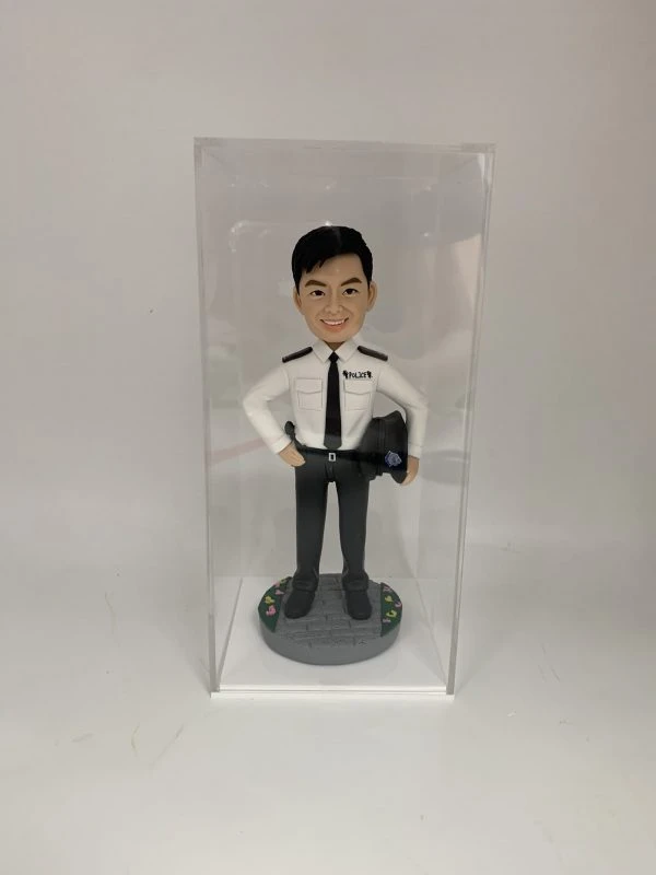 這是一份意義非凡的【晉升】賀禮，為一位年輕的【警務人員】訂製的專屬【人像公仔】。 從公仔的制服細節——尤其是肩上的一條銀色橫柴——我們可以推斷，這位【警務人員】榮升的職位是「見習督察」，這是其警隊生涯一個光輝的起點。公仔自信的笑容與輕鬆的站姿，正是這份喜悅的最佳寫照。 作品設計簡潔而專注，將所有焦點都集中在主角身上，底座的小花點綴，則象徵著他未來職業道路的無限生機。 這份禮物不僅僅是一件擺設，它更是一份認可、一個見證，紀念著他通過努力，成功邁入警官行列的決定性時刻。