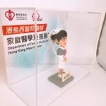 訂製醫護人像公仔，身穿白色護士制服與帽子，佩戴眼鏡，站立於底座上，背後展示「港島西醫院聯網、家庭醫學及基層醫療部門」標誌。此公仔為香港西醫院聯網家庭醫學及基層醫療部的專屬醫護造型禮物，象徵醫生與護士的專業精神，適合作為醫護感謝禮物或退休紀念品。