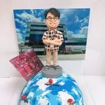 一款慶祝海外店開張的禮物，一位男士人像公仔站在標示了多個國家的地球模型上，背景是公司大樓照片，並搭配電路板圖案，是一款象徵全球擴展的開張禮物。