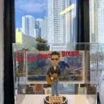 台灣歌手優客李林（林志炫）的訂製人像公仔，公仔戴著太陽眼鏡並抱著結他，其背景配件裝飾為一張復古風格的演唱會海報。