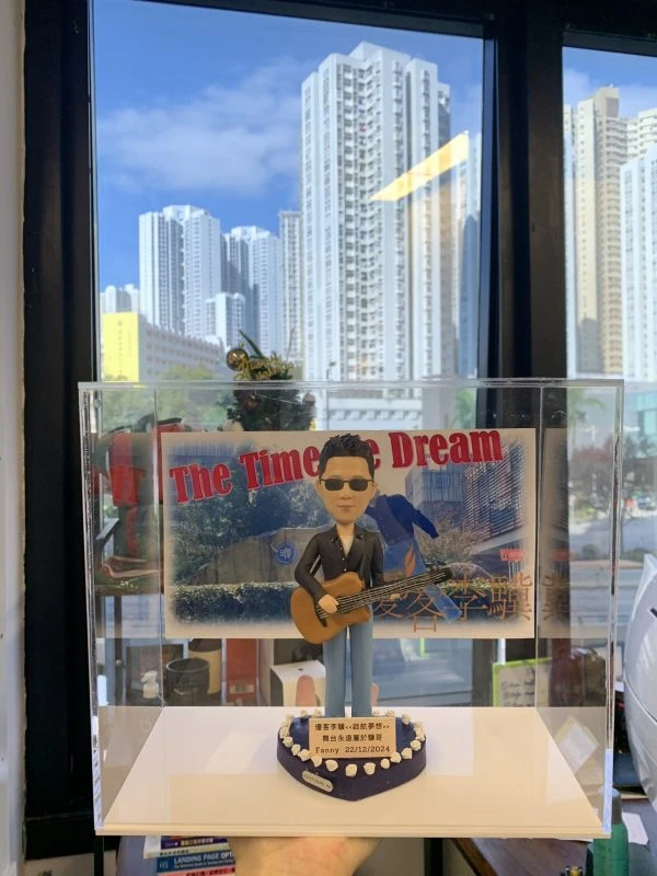 台灣歌手優客李林（林志炫）的訂製人像公仔，公仔戴著太陽眼鏡並抱著結他，其背景配件裝飾為一張復古風格的演唱會海報。