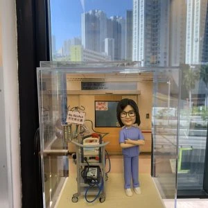 一款專屬定製的醫護人像公仔，身穿藍色護理制服，雙手交叉站立於醫療場景中。背景標示「深切治療部 (ICU)」，公仔旁邊擺放有醫療推車、監護設備與插管機，場景真實還原重症監護室環境。底座刻有「Constance Hau Ling Happy Retirement」字樣，作為醫生與醫護退休禮物極具紀念價值。