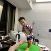 一尊動作姿態的曲棍球人像公仔，站在草綠色方形地台上，雙手握著黑色曲棍球棍，準備擊打腳前的白色球。公仔穿著紅藍白相間的球衣與短褲，胸前與褲上印有數字「80」及圓形隊章樣式，右腿配戴紅色護襪，腳穿黃色球鞋。地台前方名牌寫有「Dr. Alex W.K. CHAN」。背景為室內工作室環境，牆上有白板與貼紙。此作品屬人像公仔與曲棍球人像公仔的訂製運動主題擺設。