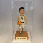 籃球員主題人像公仔：短髮少年公仔身穿白色籃球球衣與球褲，胸前有金邊字母標誌，腳踩灰色球鞋；右手持橙色籃球、左腳邁步向前的運球姿勢。公仔站在橘棕色方形底座上，前方銘牌寫有「Chuck 18岁 生日快乐！」字樣；整體置於透明展示盒中，白色背景簡潔，呈現適合作為生日禮物的籃球主題人像公仔。