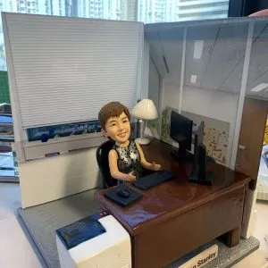 老闆｜退休禮物｜人像公仔推薦：女老闆公仔坐在辦公椅後，搭配深棕辦公桌、雙螢幕、鍵盤滑鼠與印表機，背景為玻璃隔間與百葉窗，名牌標示公司名稱，完整呈現她的辦公室日常；支援客製姓名、職銜、年份與場景配件，將專業與回憶一次收藏。Keywords：老闆，退休禮物，人像公仔。