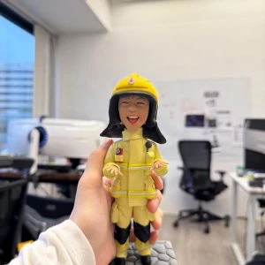 一款為消防員訂製的Q版人像公仔，公仔面帶燦爛開朗的笑容，身穿全套黃色消防制服，站立在刻有個人編號PFn11195的石磚底座上，是一份充滿活力的退休禮物。