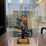 一款祝賀女警務人員晉升的人像公仔禮物，公仔身穿警察制服並懷抱一隻柴犬寵物，背景是警察總部大樓照片。底座銘牌記錄了這次晉升的職級與日期。