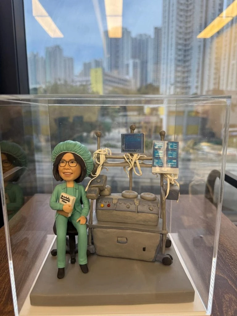 訂製醫生人像公仔｜醫護人員身穿綠色手術服及手術帽，坐在麻醉機旁，背後連接多個醫療監測屏幕與管線，細緻還原手術室場景。專屬醫生的醫護紀念公仔，適合作為禮物或退休紀念品。