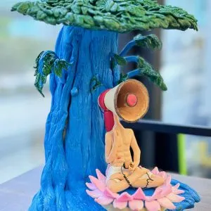 一款超現實主義的動漫人物人像公仔，一個喇叭頭的男子在藍色大樹下的蓮花上冥想，是充滿藝術感的獨特生日禮物。