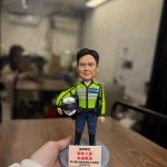 一款為香港交通部警務人員訂製的榮休人像公仔。該警員身穿螢光綠色交通制服，手持電單車頭盔。底座銘牌刻有「榮休之喜」及贈送單位「東九龍交通部執行及管制組」。