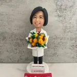 定製醫護人像公仔，角色為實驗室主管 Ms Law Wai Yin，身穿白袍，手捧鮮花，底座刻有「Laboratory Manager」字樣。此公仔象徵醫護專業及實驗室醫生/醫療管理人員的專業身份，是醫院或科研機構專屬的退休與感謝禮物。