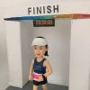 一位女跑手的運動公仔，她正在衝過終點線，終點門上的計時器顯示時間為03:30:00，是一份慶祝個人紀錄的健身禮物。