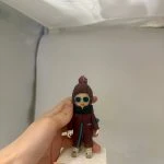 手持底座的小朋友主題人像公仔：戴針織毛帽與墨綠連帽圍脖、穿酒紅色連身外套與運動鞋的bb造型，臉上配藍框圓形墨鏡，站在白色發泡底座上；底座前緣橘色標籤寫有「2歲 生日快樂 Gabriel」字樣；背景為簡潔棚拍白色。